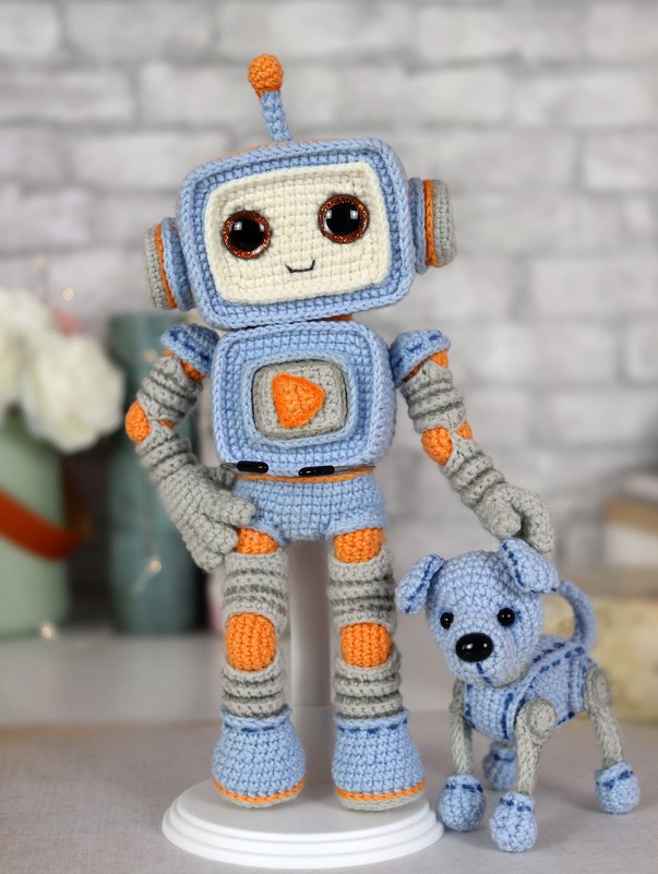 Blue, gray and orange crocheted amigurumi robot standing beside a small matching crocheted dog.