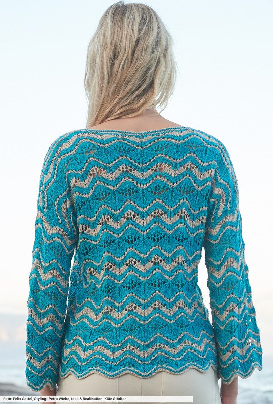 Rückansicht einer Frau in einem türkisen und beigen Strickpullover mit Wellen‑Lochmuster.
