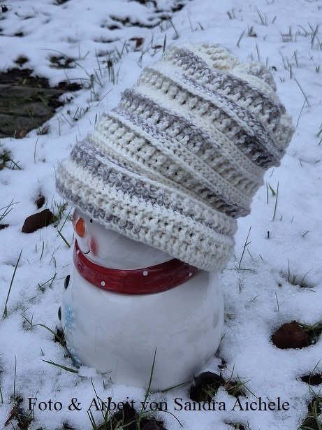 Gehäkelte Damenmütze in Creme und Grau auf Schneefigur im Freien