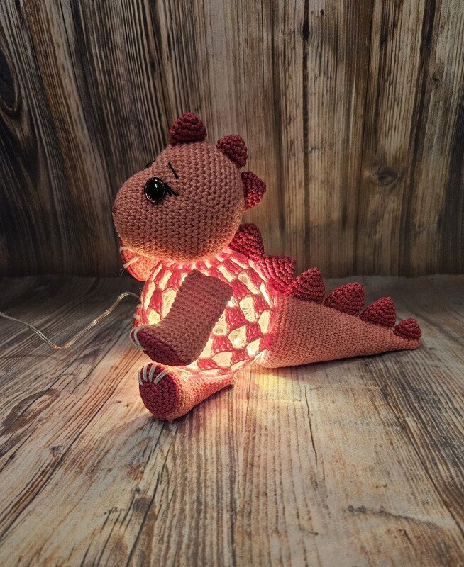 Gehäkelter rosa‑pfirsichfarbener Amigurumi‑Drache mit leuchtender, offener Mittelpartie