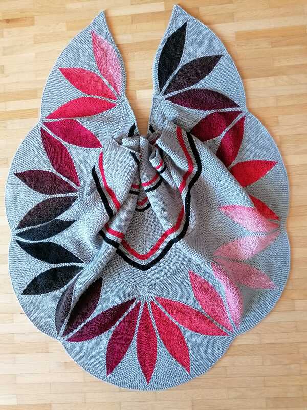 Gestricktes hellgraues Dreieckstuch mit roten und schwarzen Blattmotiven auf Holzboden