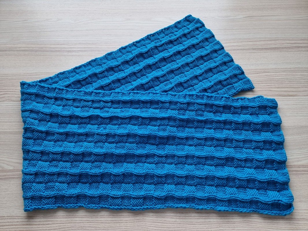 Blauer gestrickter Schal mit reliefartigem Blockmuster auf hellem Holzuntergrund