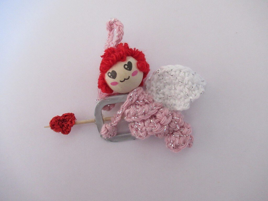 Gehäkeltes Amigurumi-Engelchen rosa mit weißen Flügeln und rotem Herzpfeil