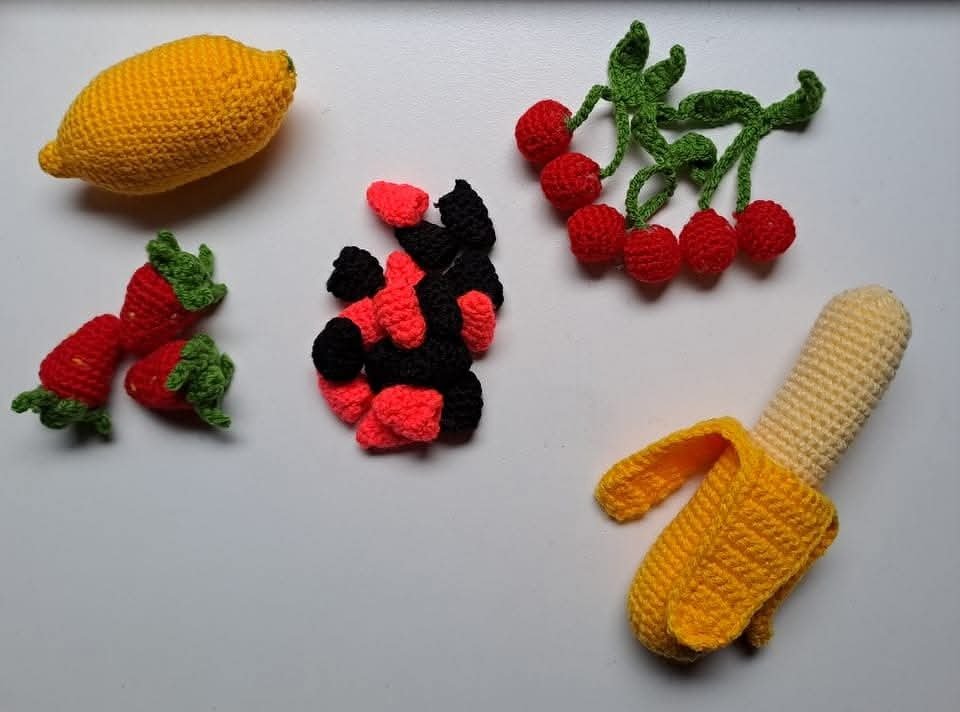 Crocheted grocery play set with lemon, peeled banana, strawberries, cherries, and mixed berry pieces on a white background