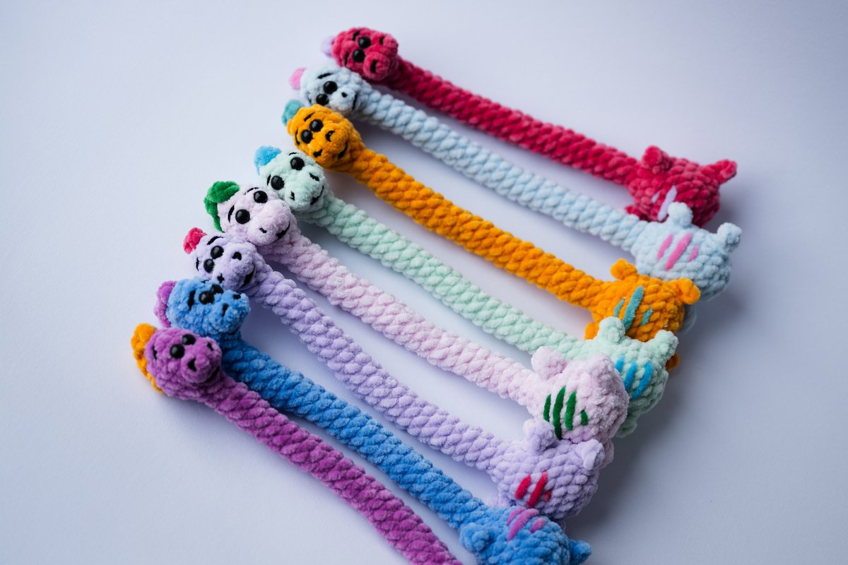 Reihe gehäkelter pastellfarbener Dino- und Drachenfiguren mit langen Kordeln