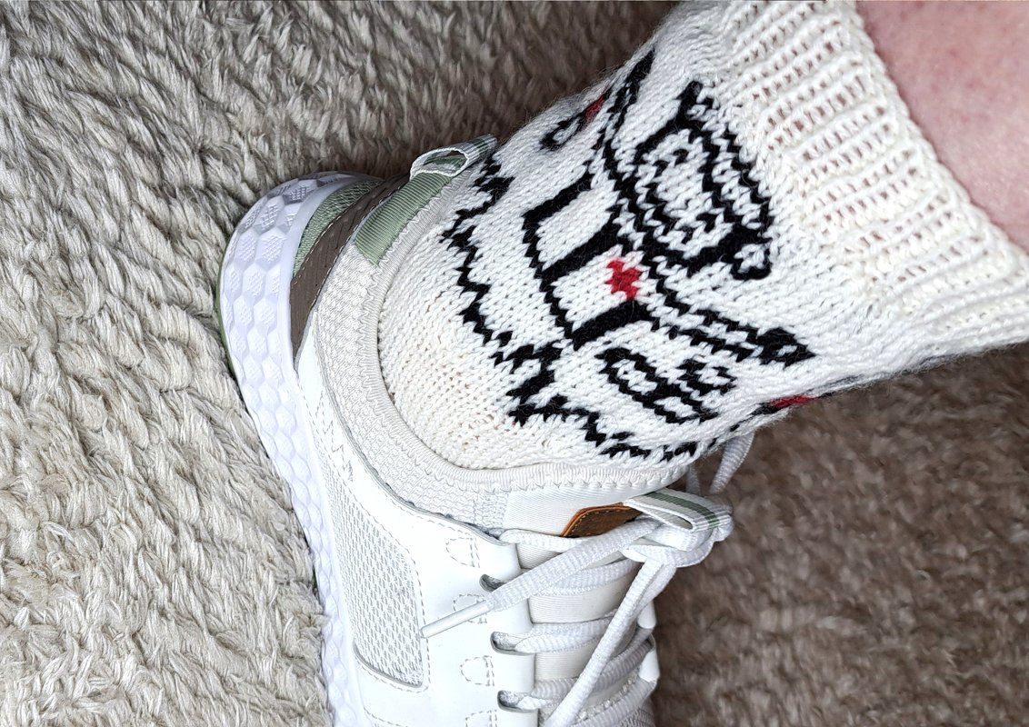 Close-up of white knitted sock with black and red geometric motif worn with a white sneaker.
