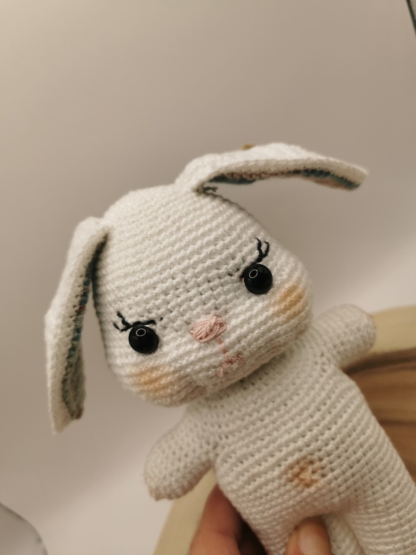 Nahaufnahme eines weißen Amigurumi-Hasen mit Fokus auf Maschen, angenähte Augen und Ohren