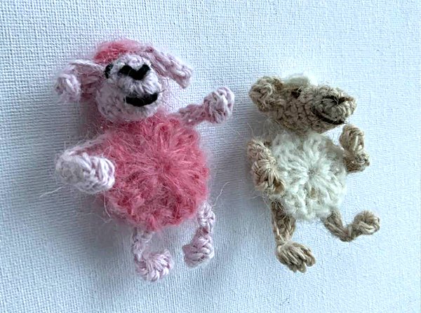 Zwei pastellfarbene handgehäkelte Schäfchen, eines rosa und eines beige, auf hellem Hintergrund