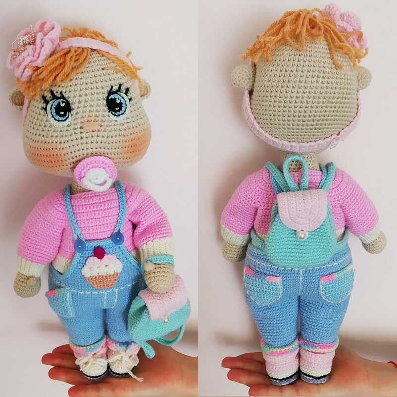 Front and back views of a crochet amigurumi doll wearing blue cupcake overalls, pink sweater, pacifier, floral headband and small mint backpack