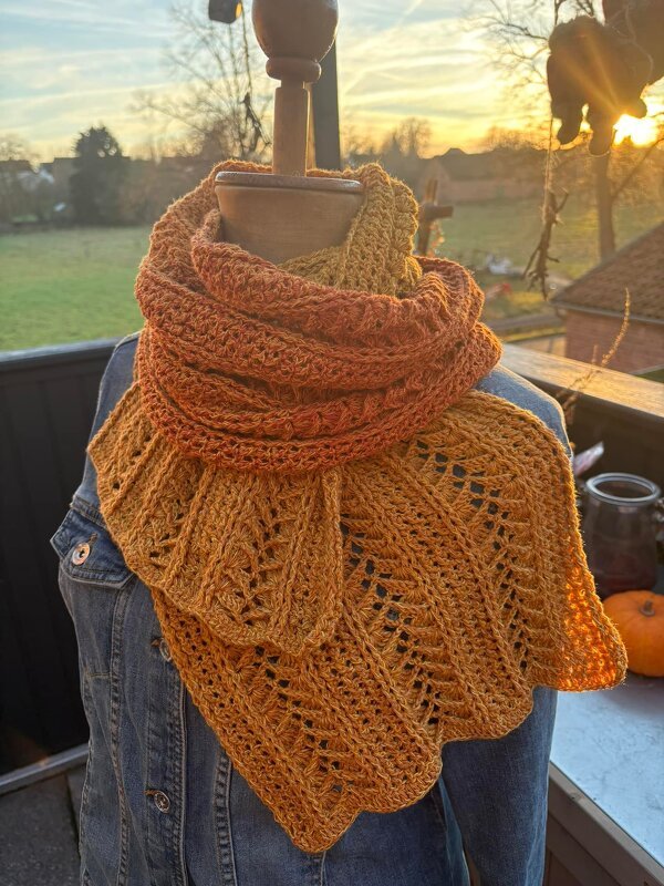 Crocheted orange and gold lace scarf draped on a mannequin wearing a denim jacket at sunset.