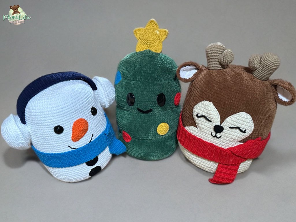 Drei gehäkelte Weihnachtskissen: Schneemann mit blauem Schal, Tannenbaum mit Stern und Rentier mit rotem Schal