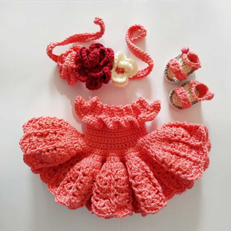 Korallenfarbenes gehäkeltes Puppenkleid mit Rüschen, Blumenstirnband und kleinen Sandalen