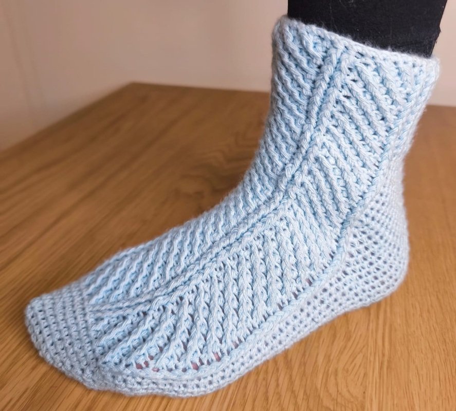 Detailansicht einer hellblauen gehäkelten Socke mit diagonalen Rippen und wabenartiger Fersenstruktur