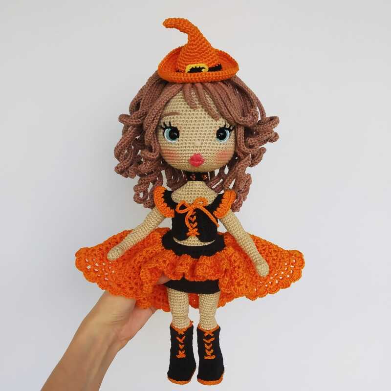 Crocheted amigurumi witch doll with orange pointed hat, ruffled skirt and black boots.