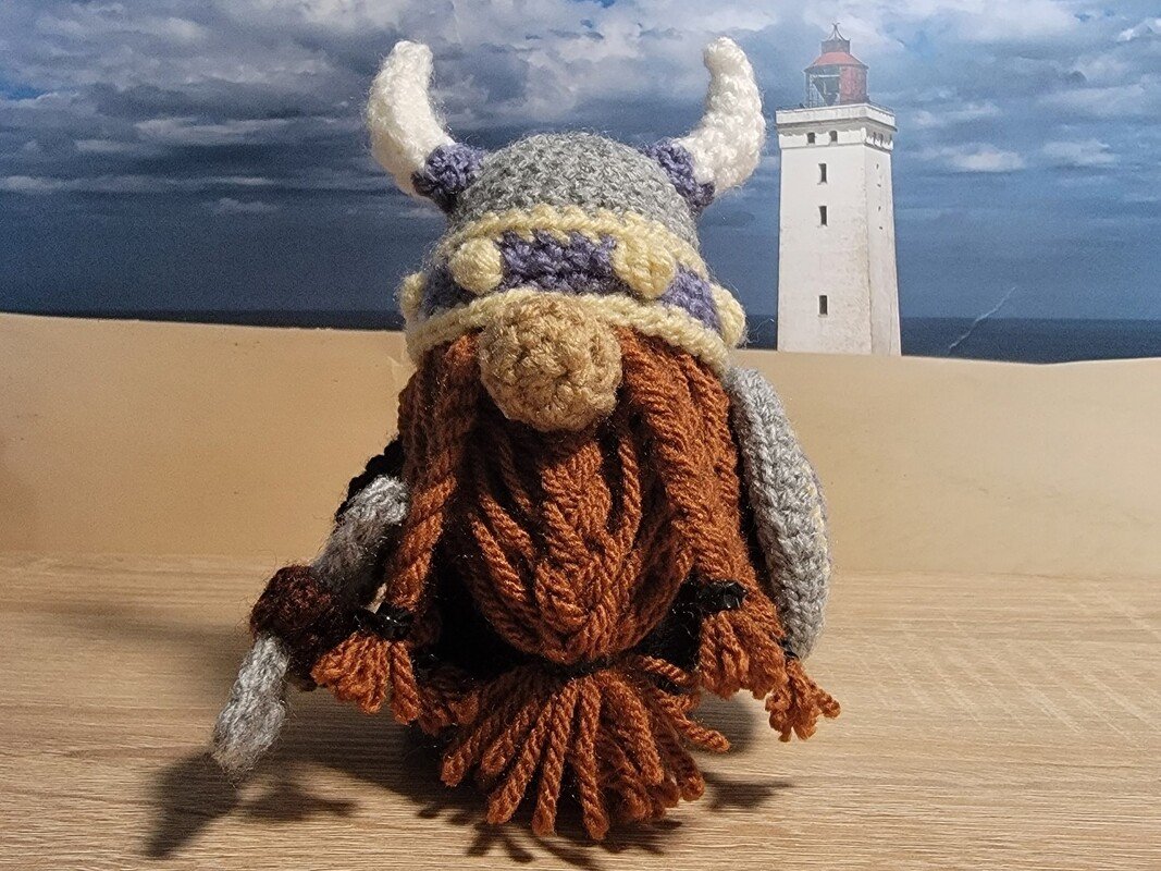 Gehäkelter Wikingernickel mit Hornhelm und braunem Bart vor Leuchtturm-Kulisse