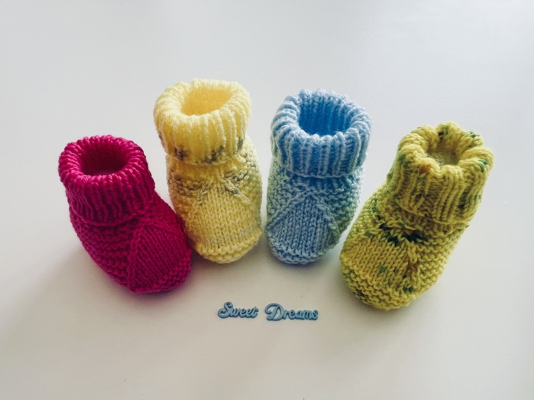 Vier farbige gestrickte Babyschuhe (Pink, Gelb, Hellblau, Grün) auf hellem Untergrund mit 'Sweet Dreams'-Schriftzug