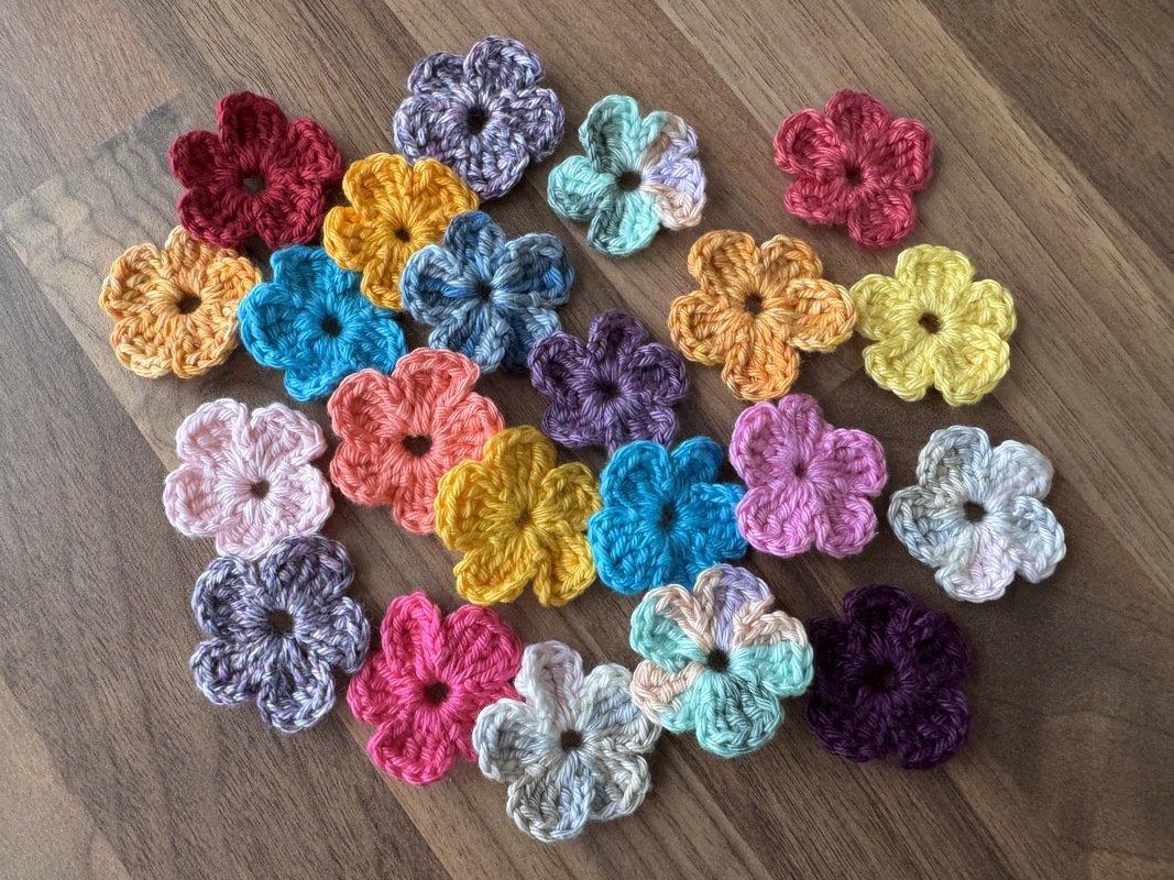Viele kleine, schnell gehäkelte Mini‑Blüten in verschiedenen Farben auf Holz