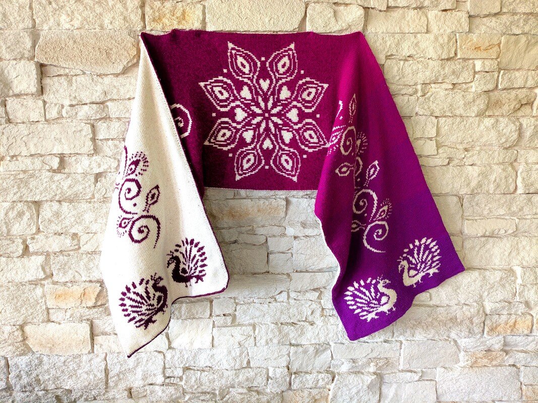 Reversible magenta and ivory bridal shawl with central floral medallion and peacock border motifs draped on a stone wall