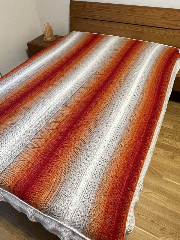 Striped crochet bedspread with alternating orange and white textured stitch bands