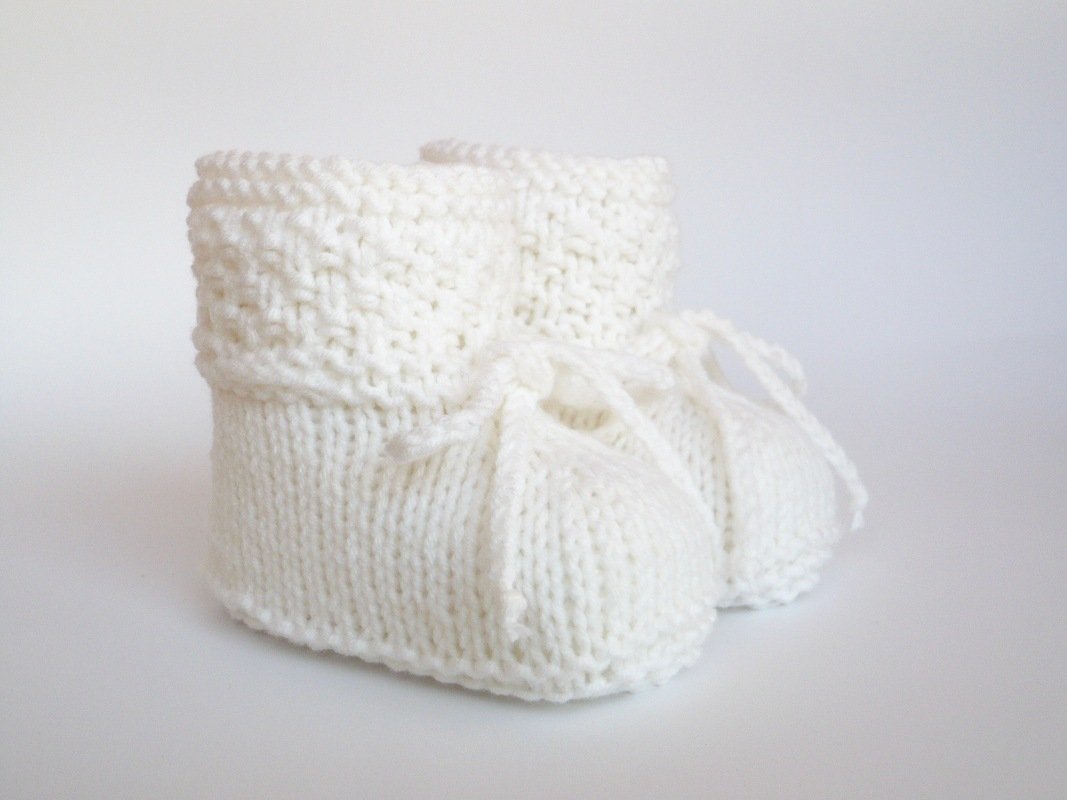 Weiße gestrickte Babyschuhe mit Umschlag und Bindeband