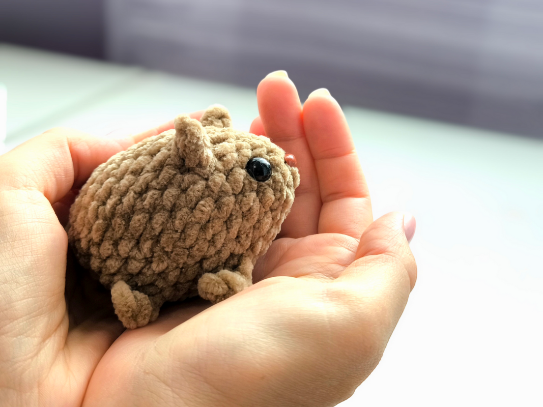 Kleines texturiertes Amigurumi-Igelchen in Händen mit glänzenden Augen