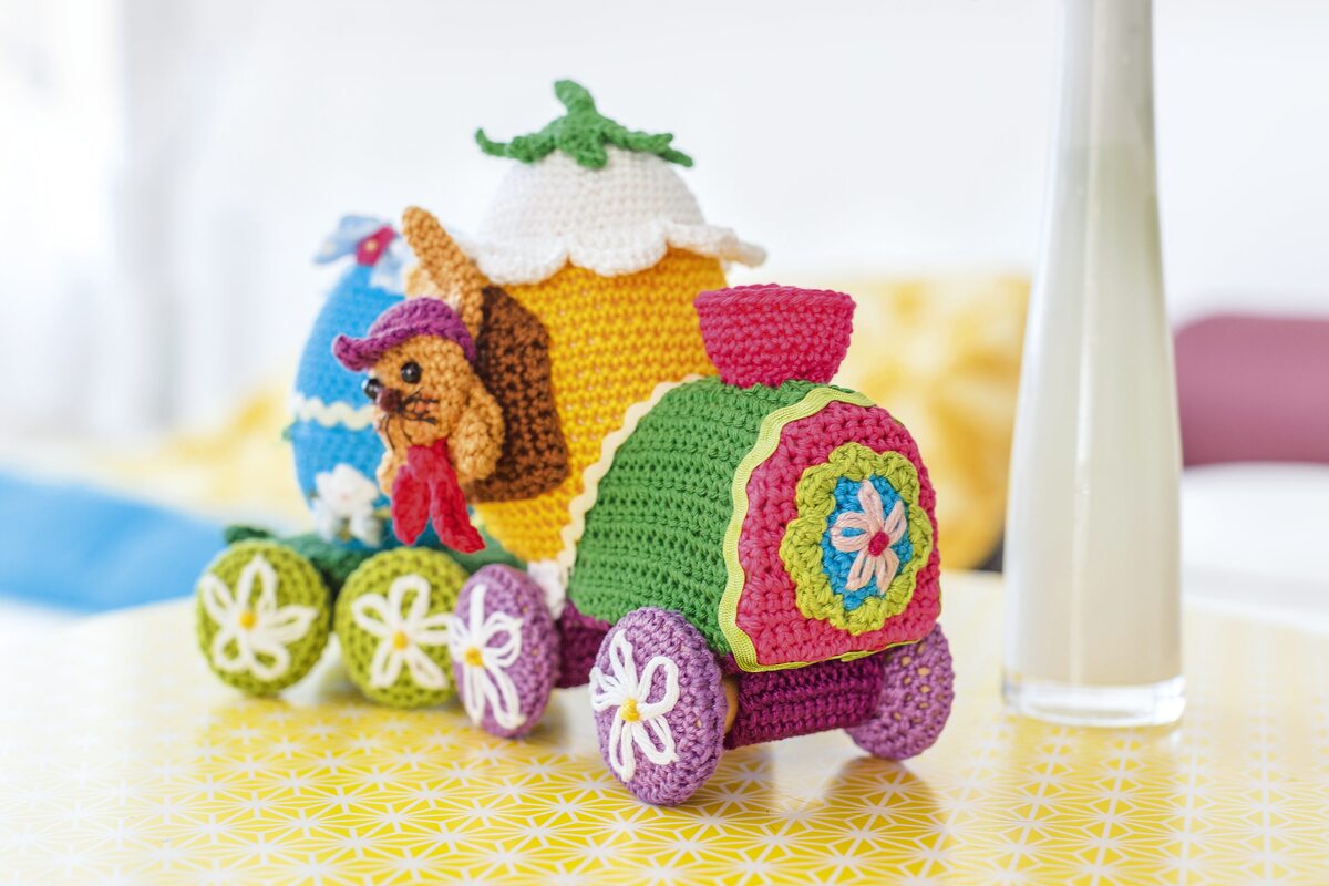 Bunter gehäkelter Deko-Zug mit Osterei-Wagen, kleiner Tierfigur und blütenverzierten Rädern