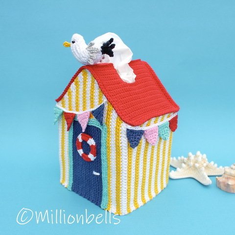 Crochet beach hut tissue box cover with red roof, yellow-and-white stripes, blue door, and seagull tissue dispenser.