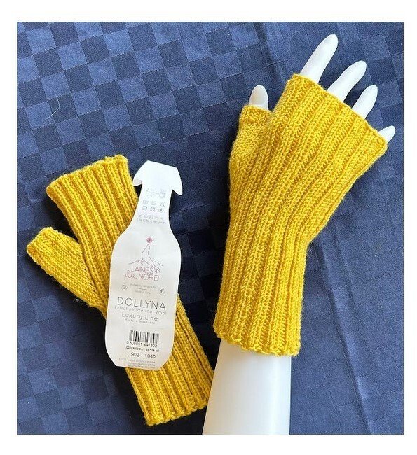 gelbe gestrickte fingerlose Armstulpen im Rippenmuster auf dunklem Hintergrund mit Garnetikett