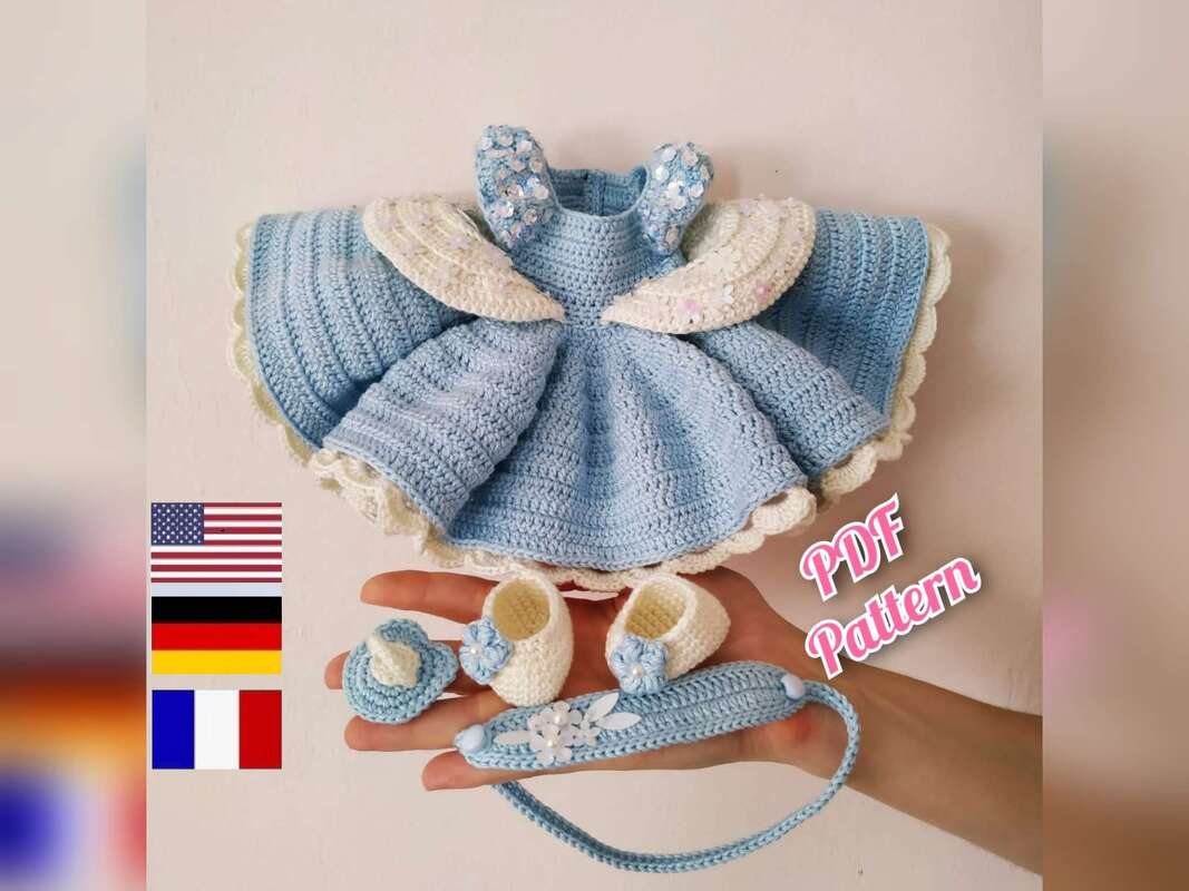 Light-blue crocheted amigurumi dress, two booties, pacifier, and headband shown in a hand