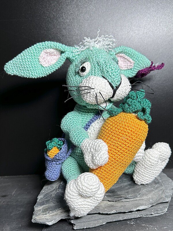 Gehäkelter mintgrüner Amigurumi-Hase mit großer oranger Karotte und kleinem blauen Täschchen