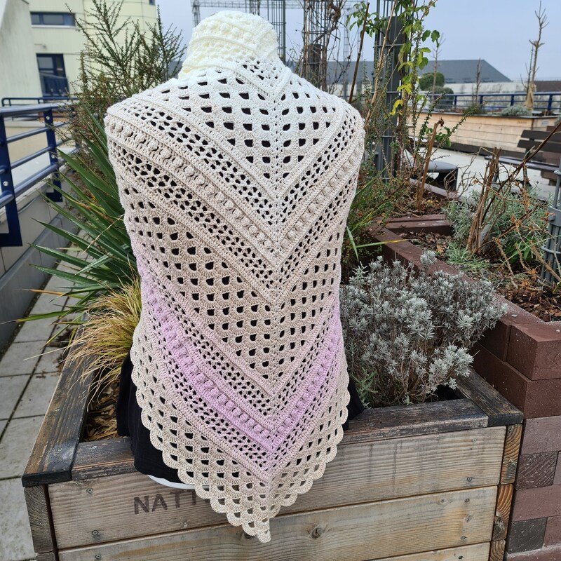 Crocheted triangle shawl in white, beige and pink gradient with lace and bobble stitches on a mannequin.