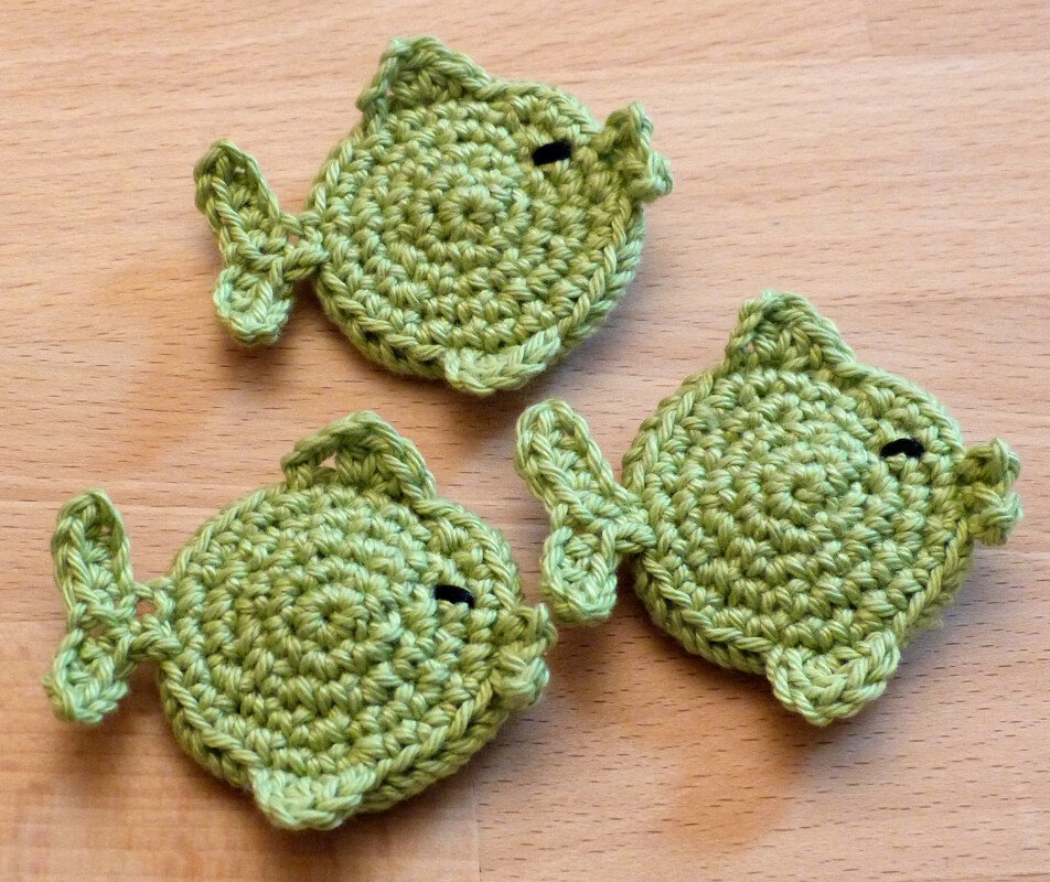 Drei runde gehäkelte Fische in Grün, dekorativ angeordnet