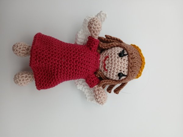 Gehäkeltes Amigurumi-Engelchen im roten Kleid mit weißen Flügeln, braunen Haaren und gelbem Heiligenschein auf weißem Hintergrund.