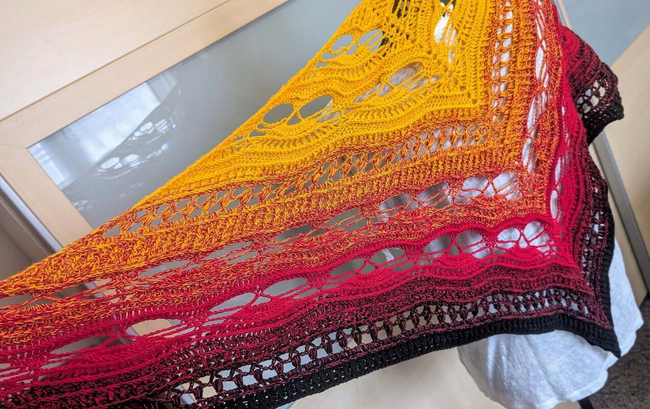 Crocheted triangle shawl with yellow, orange and red gradient and openwork stitches