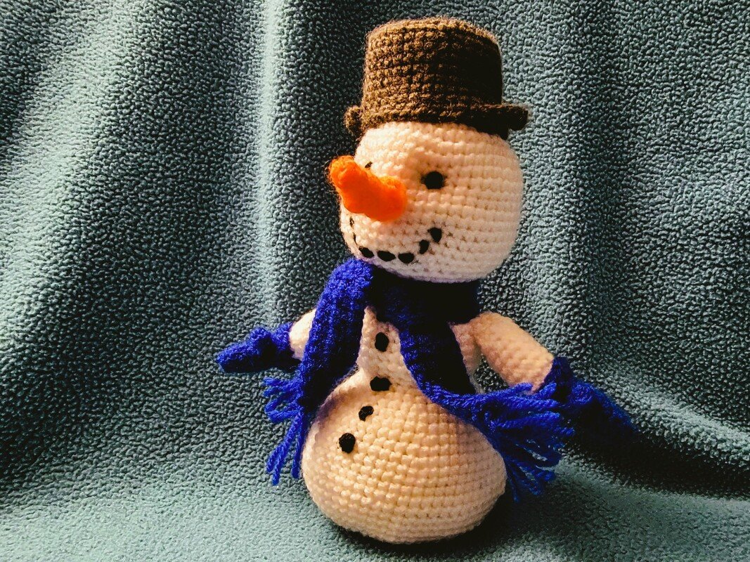 Gehäkelter Amigurumi-Schneemann mit braunem Zylinderhut, blauem Schal und Karottennase