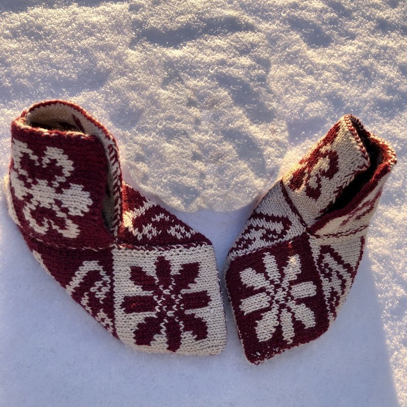 Rot-weiße gestrickte Hausschuhe mit Schneeflockenmuster auf Schnee
