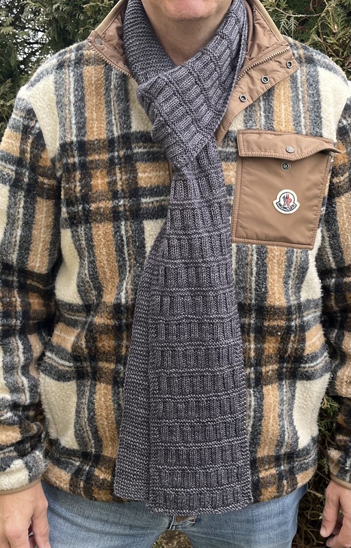 Grau gestrickter Schal mit Kastenmuster, gebunden als Schlaufe vor karierter Jacke