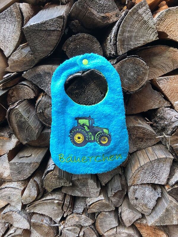 Stickmotiv: Grüner Traktor und 'Bäuerchen' auf einem blauen Lätzchen, als Anwendungsbeispiel