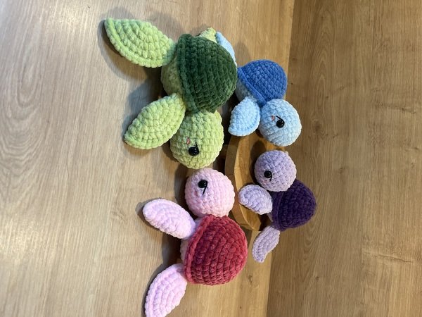 Vier gehäkelte Amigurumi-Schildkröten aus Plüschgarn auf Holzboden