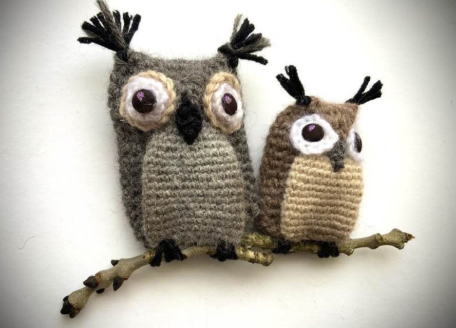 Zwei gehäkelte Amigurumi‑Eulen in Grau und Braun auf einem Ast