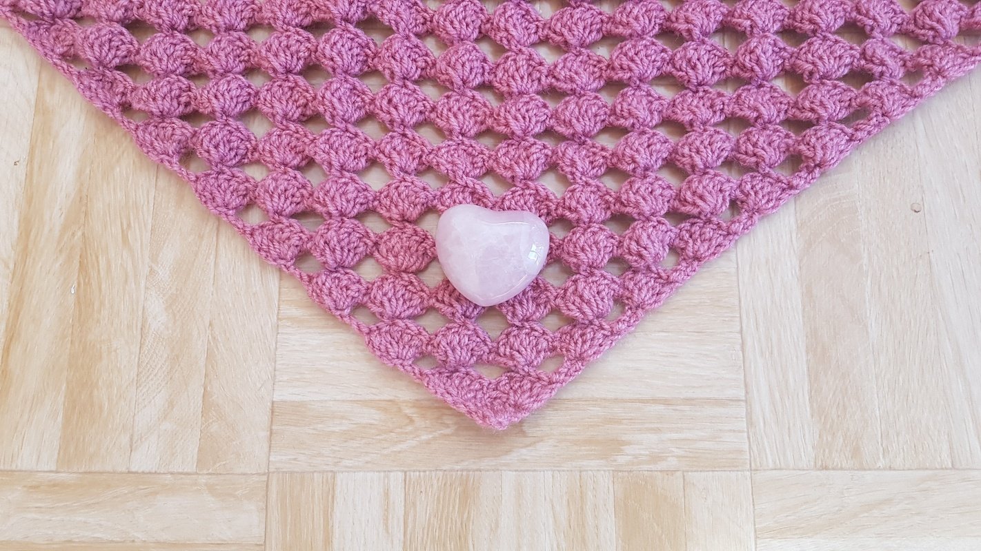 Rosé gehäkeltes Dreieckstuch mit Muschelmuster und Rosenquarz-Herz auf hellem Holzboden