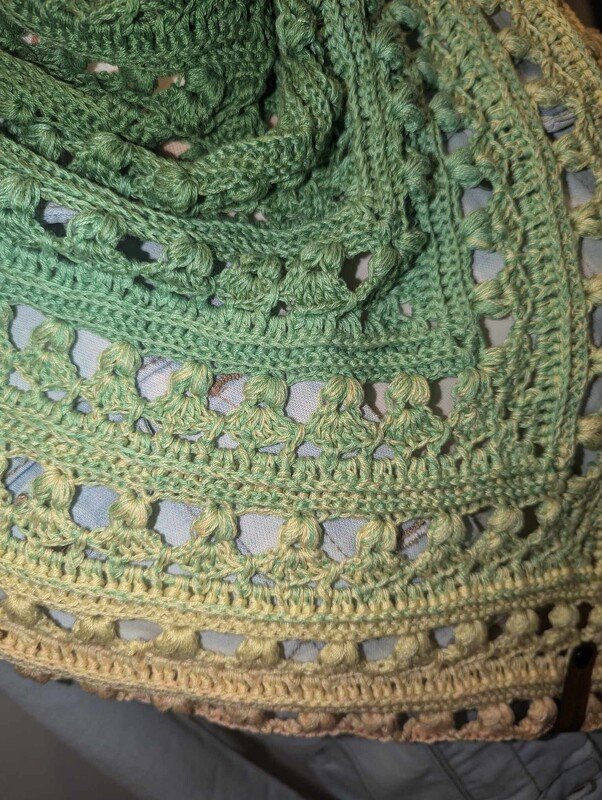 Close-up of ombre green-to-beige crocheted triangle shawl showing bobble and openwork stitches.