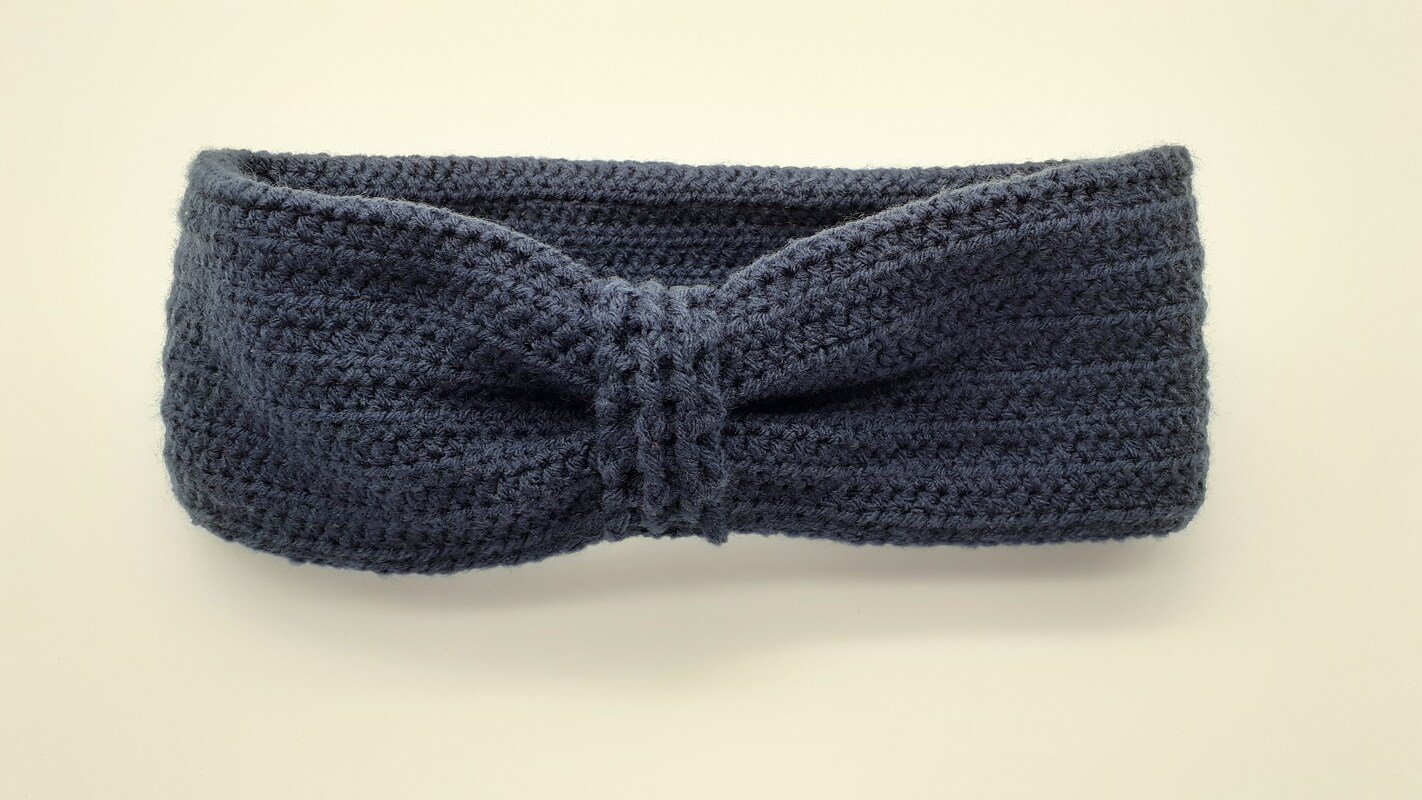 Nahaufnahme eines dunkelblauen, gehäkelten Stirnbands mit verdrehtem Knoten in der Mitte.