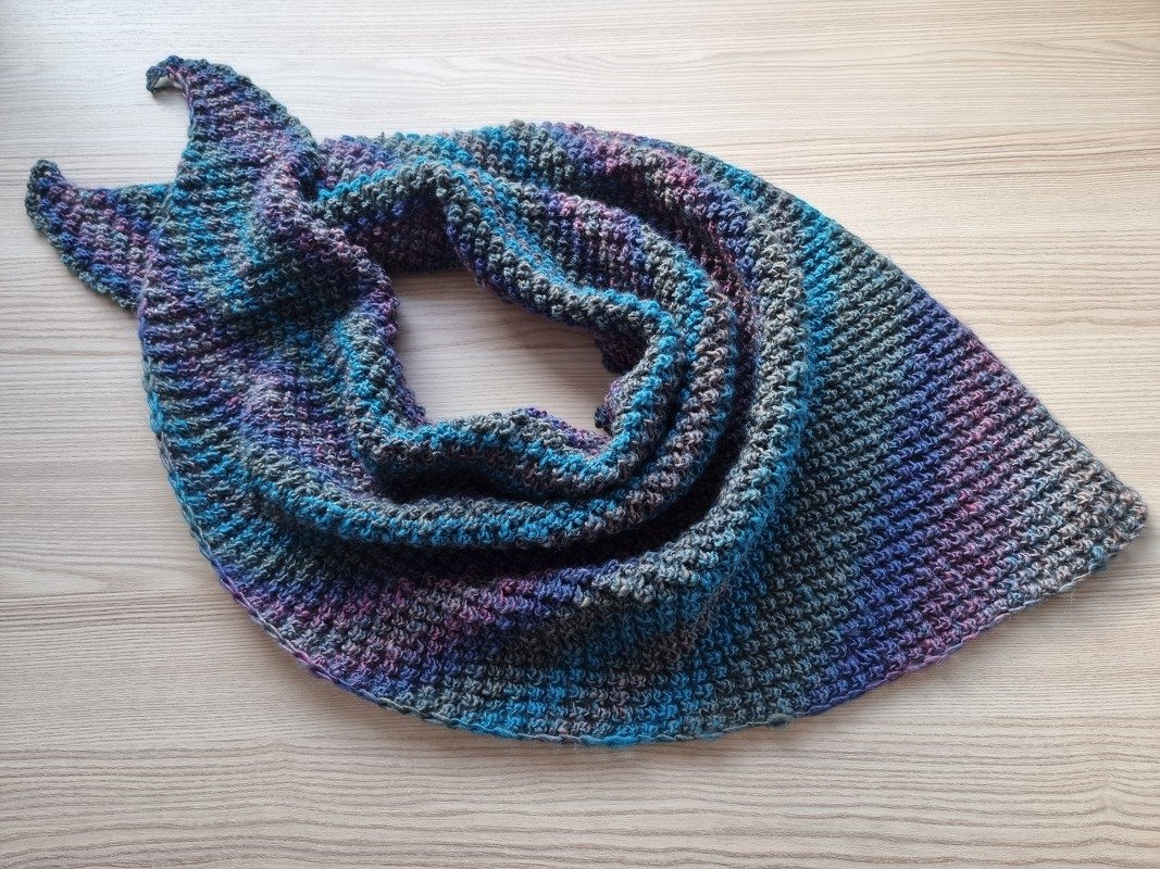 Gestricktes Dreieckstuch in melierten Blau-, Lila- und Grautönen auf hellem Holz