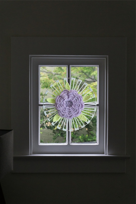 Gehäkelte lila Blume mit grünen Blättern als Fenster- oder Wanddekoration