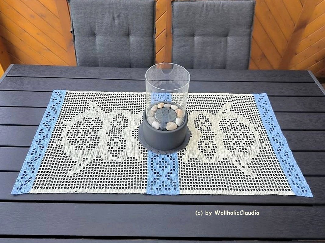 Rechteckiger gehäkelter Tischläufer in Creme mit hellblauen Borten auf dunklem Tisch, Glaswindlicht in der Mitte