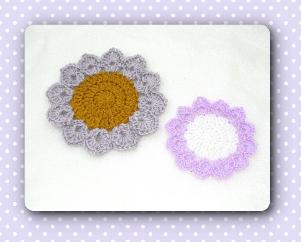 Zwei gehäkelte blumenförmige Deckchen, das größere grau mit senfgelber Mitte, das kleinere lila mit weißer Mitte.