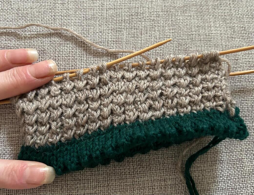 Nahaufnahme einer Strickprobe für Sockenbündchen in Beige und Grün, gestrickt im Perlmuster und Rippenbündchen auf Nadelspiel.