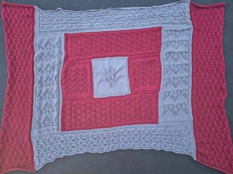 Gestrickte Patchwork-Decke in Koralle und Hellgrau, flach ausgelegt mit Loch-, Zopf- und Strukturmustern.