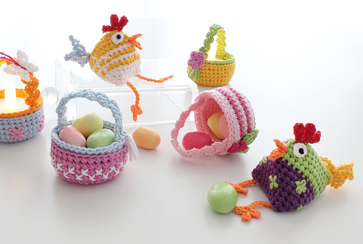 Two crocheted amigurumi chicks and four small crochet baskets with pastel eggs on a white surface.